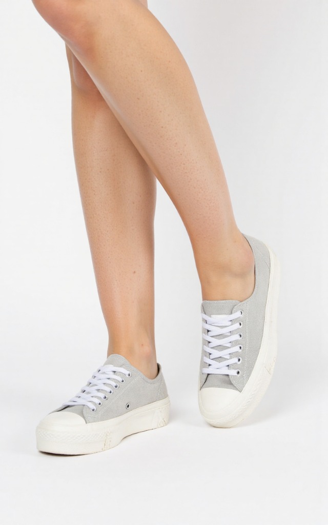 A female model wearing canvas shoes, against a white background, with a close   up of the feet